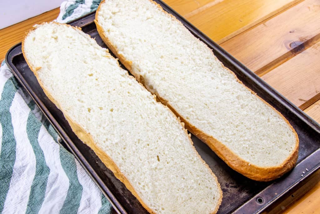 French broad loaf sliced in half lengthwise on a baking tray