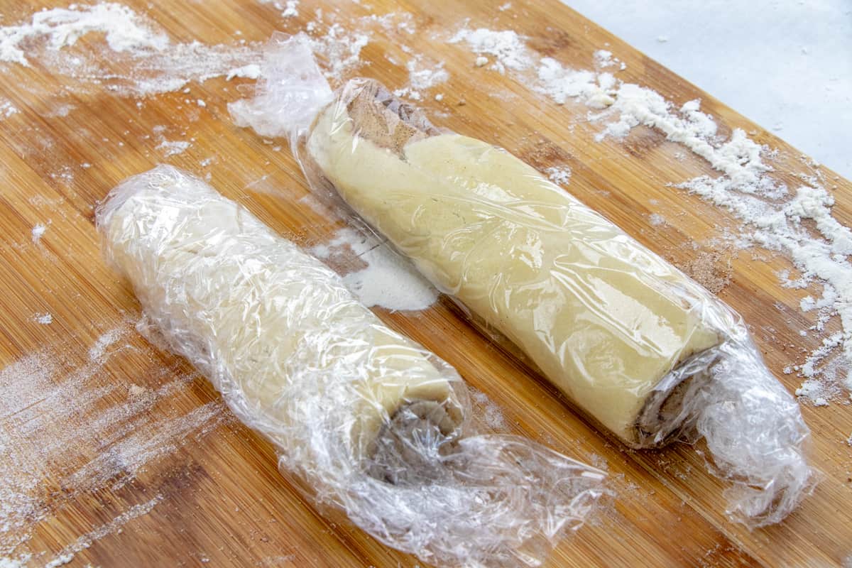 cinnamon roll cookie dough cut in half and wrapped in plastic wrap.