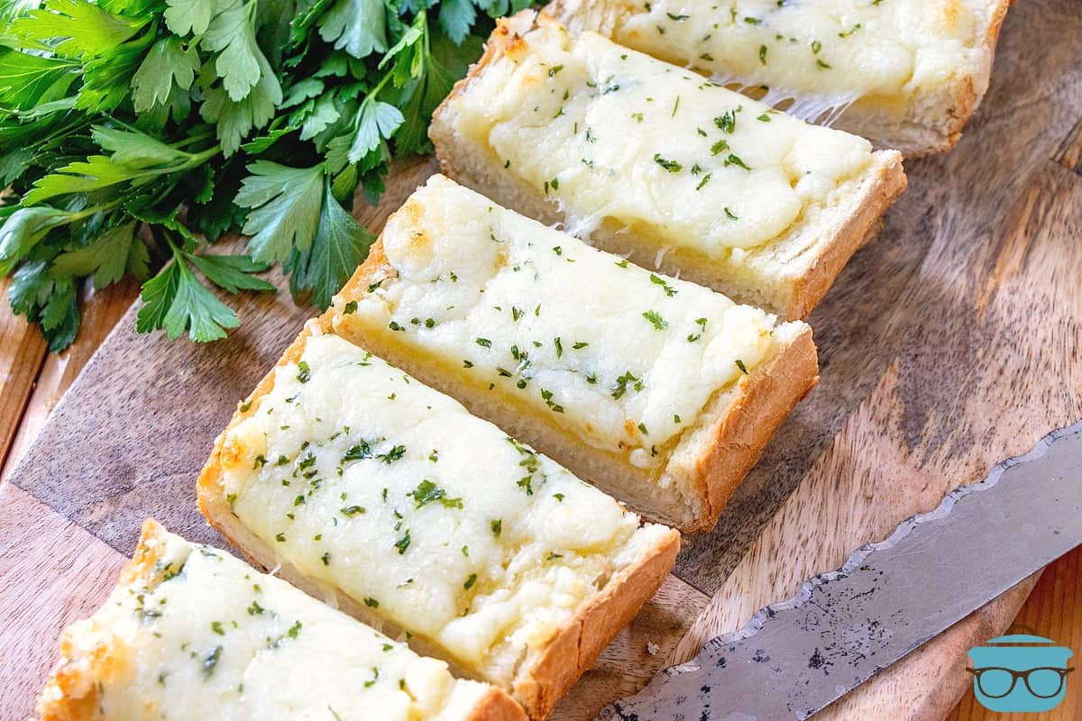 Garlic Cheese Bread, sliced on a cutting board with fresh parsley in the background.