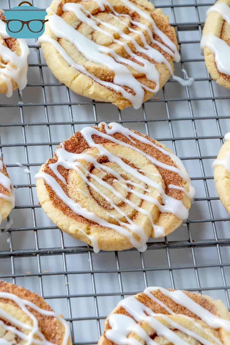 cooled cinnamon roll cookies on a cooling rack drizzled lightly with white icing.