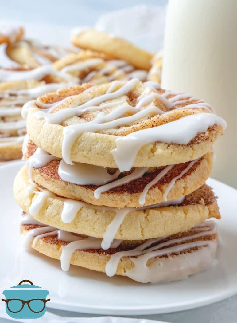 Easy Cinnamon Roll Cookies stacked four cookies high on a white plate surrounded by additional cookies.