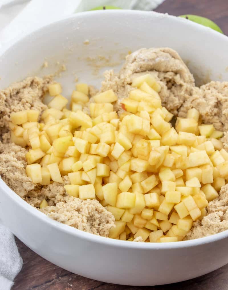 chopped apples added to snickerdoodle cookie batter in a large white bowl
