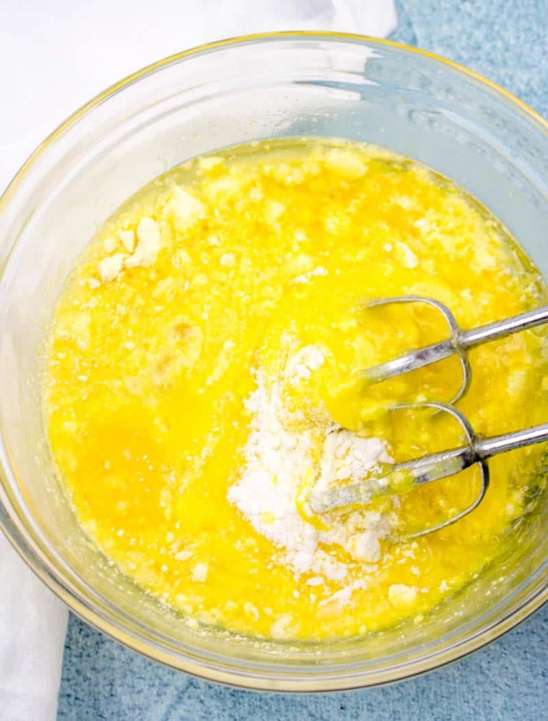lemon cake mix batter combined in a glass bowl with a handheld electric mixer.