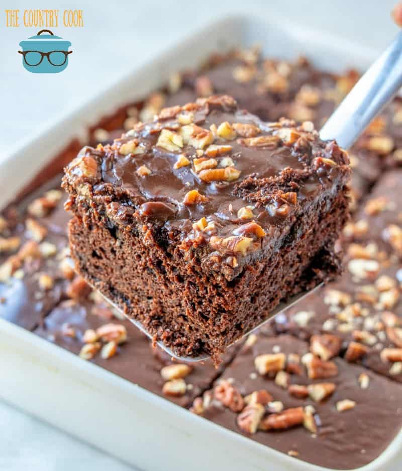 slice, double fudge Coca Cola cake with chopped pecans being held up by a spatula.