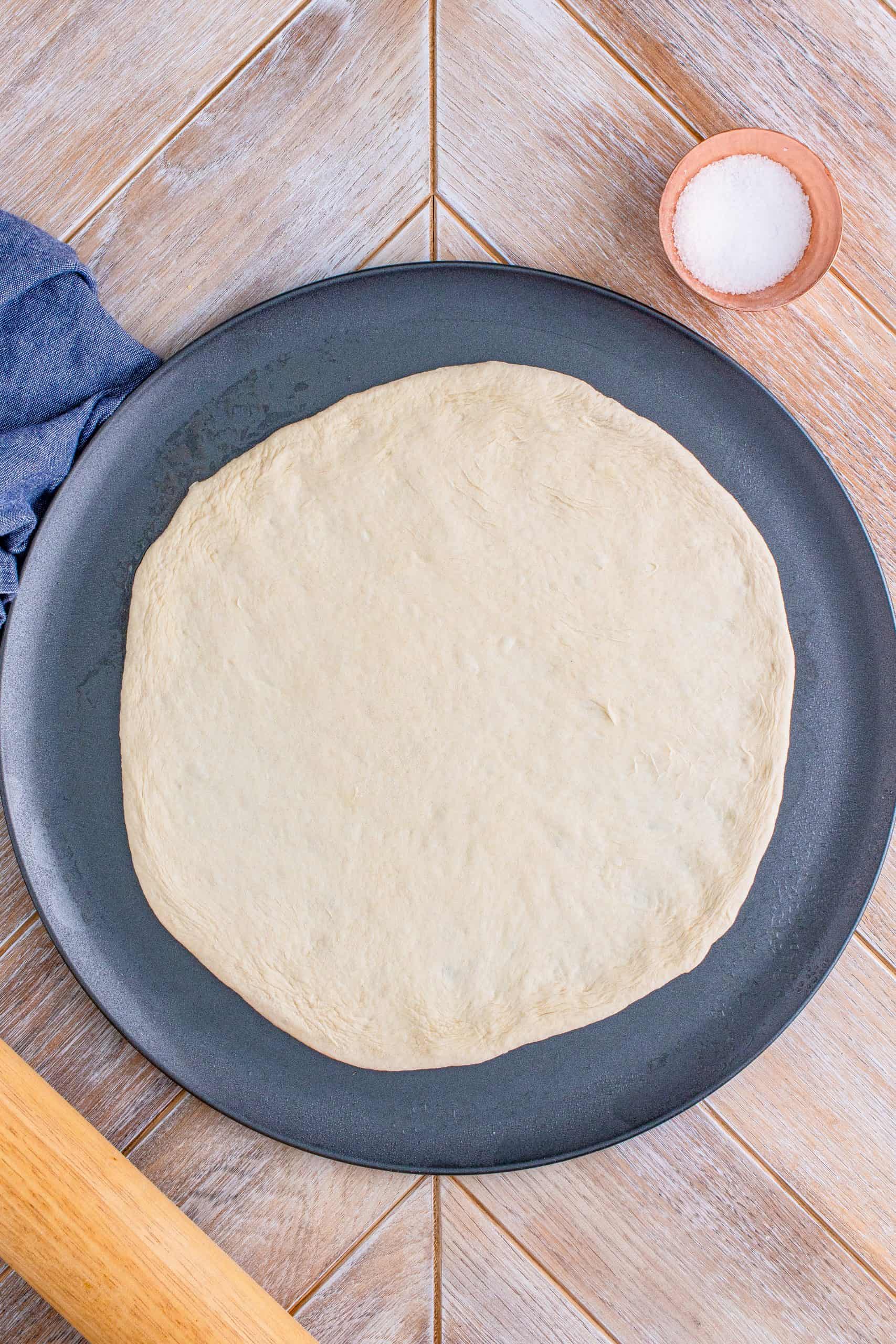 pizza dough spread out onto a greased round pizza pan.