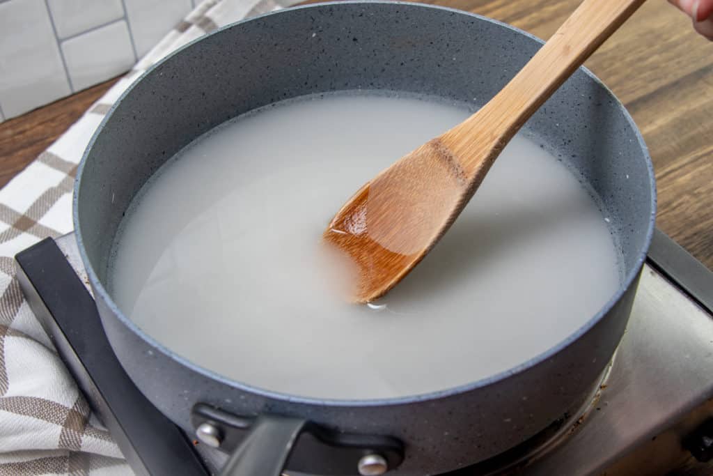 sugar and water in a large saucepan being stirred with a wooden spoon.