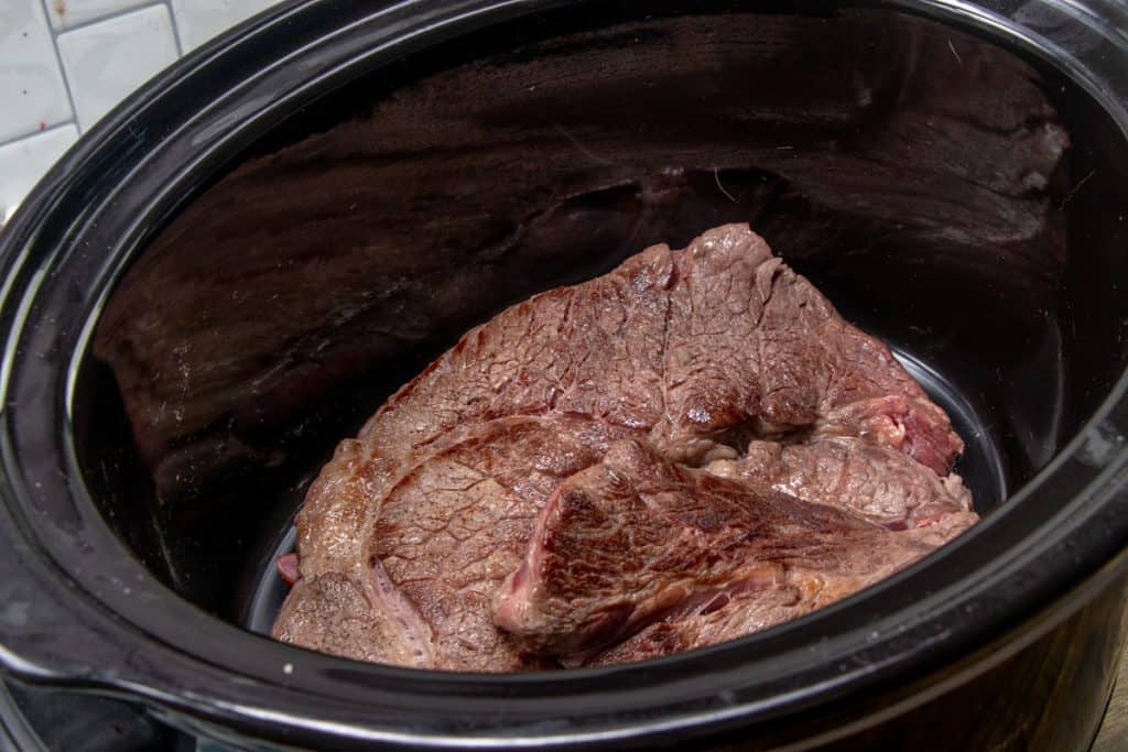 browned beef pot roast added to the bottom of an oval slow cooker.