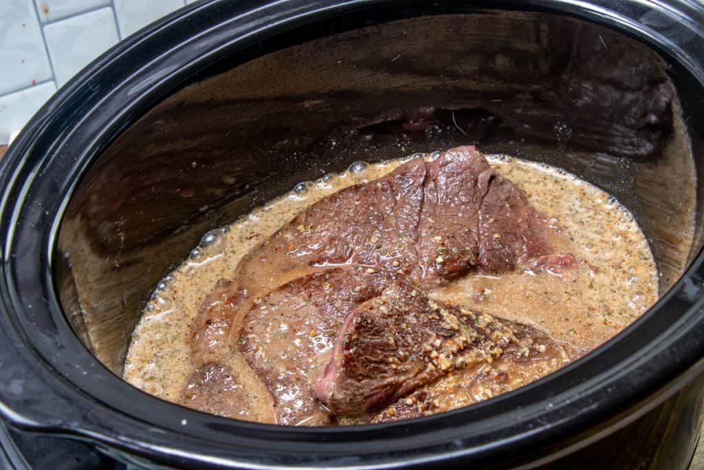 gravy mixture poured over chuck roast inside a crock pot