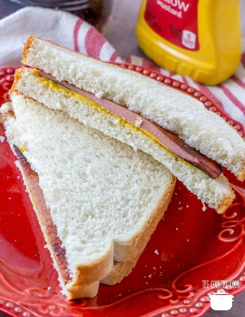 fried bologna on soft white bread with mustard, sliced in half on a red plate.