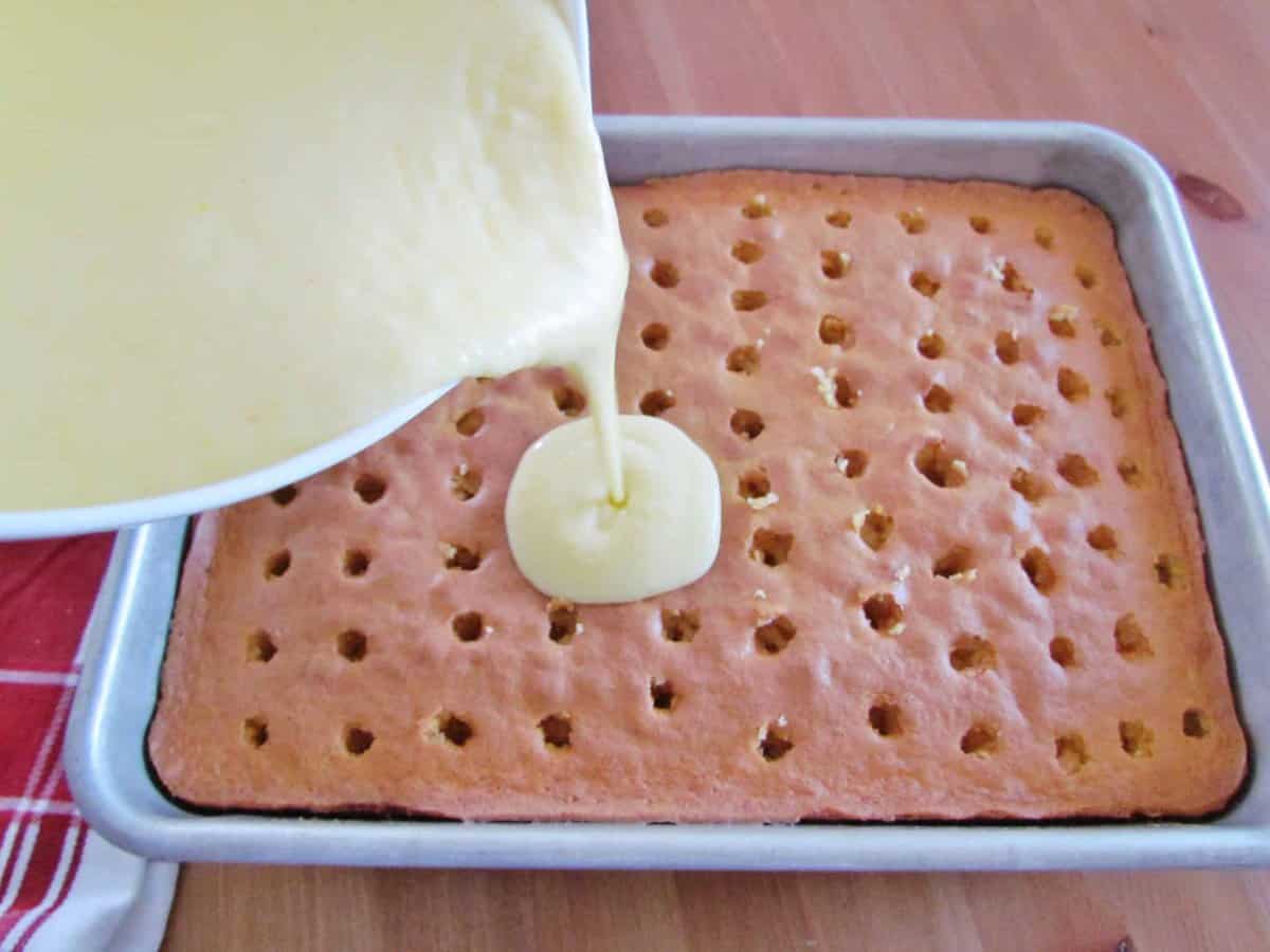pouring prepared pudding into holes of baked yellow cake.