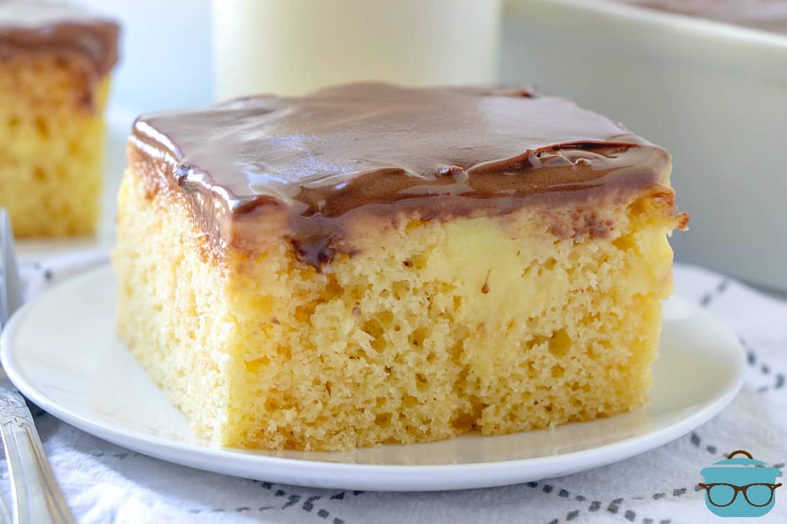 Boston Cream Poke Cake, slice on a white plate with a glass of milk in background.