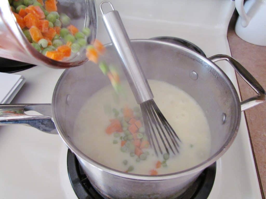 pouring in frozen peas and carrots to creamy mixture