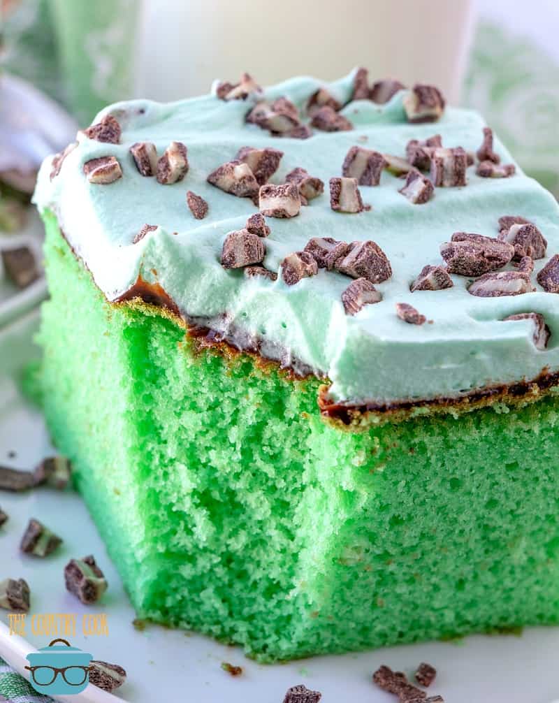 a slice of green cake with a bite removed shown on a white plate and topped with chocolate candies.