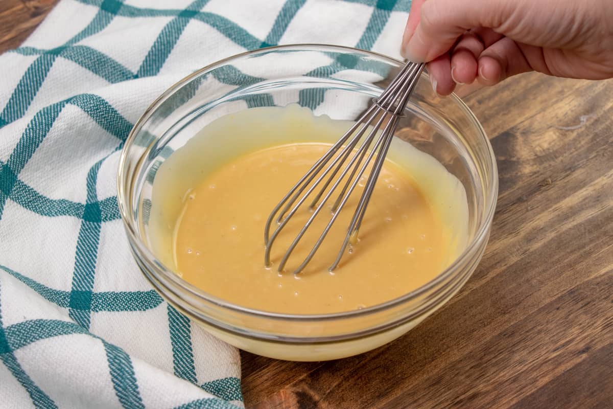 a whisk mixing together mayonnaise, dijon mustard and honey in a clear bowl.