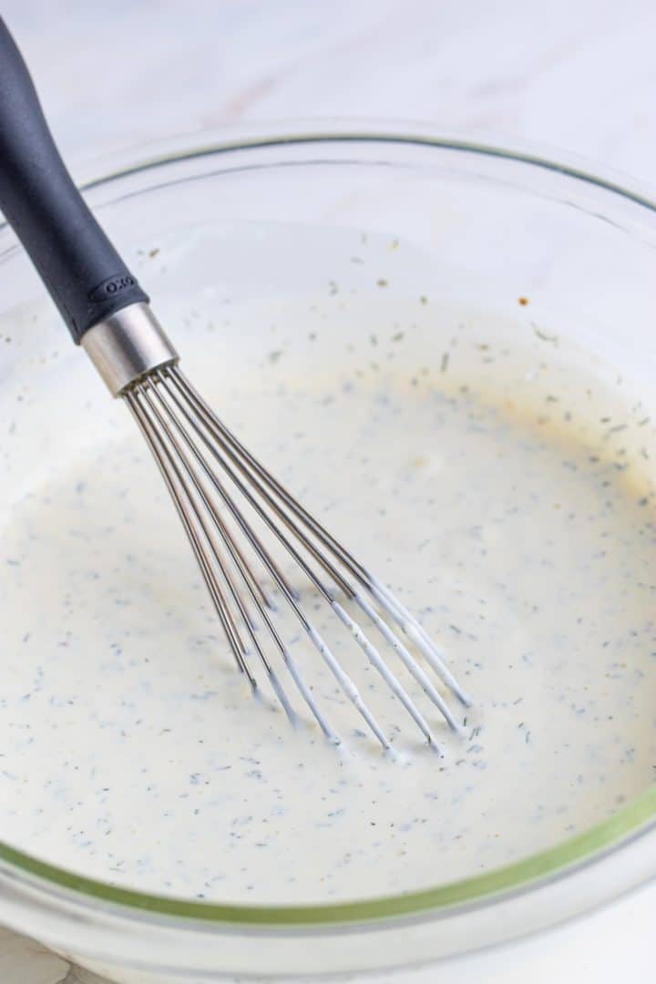 fully whisked together ranch dressing ingredients shown in a clear bowl with a silver whisk. 