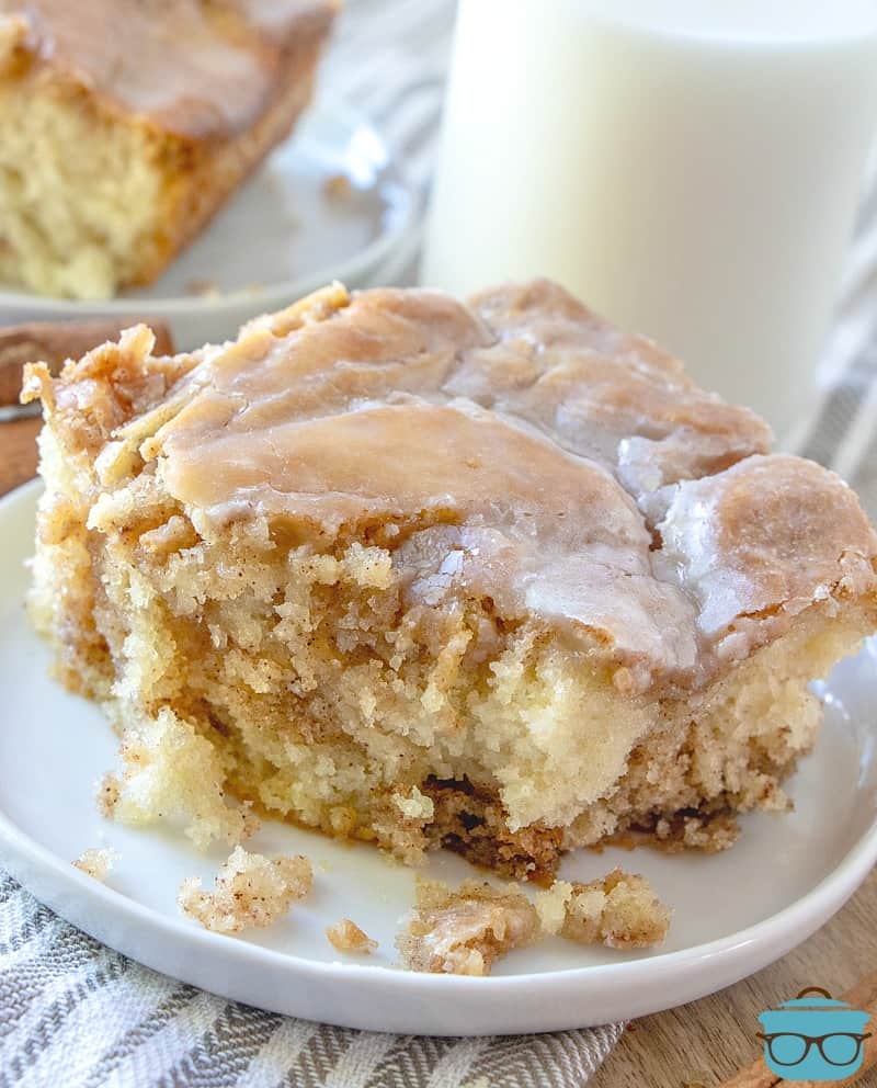 a slice of Cinnamon Roll Swirl Cake on a plate with a bite removed and a glass of milk in the background.