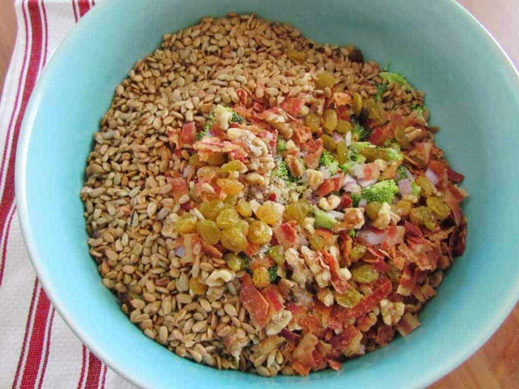 In a large bowl, add broccoli, bacon, raisins, walnuts, chopped onions and sunflower kernels.