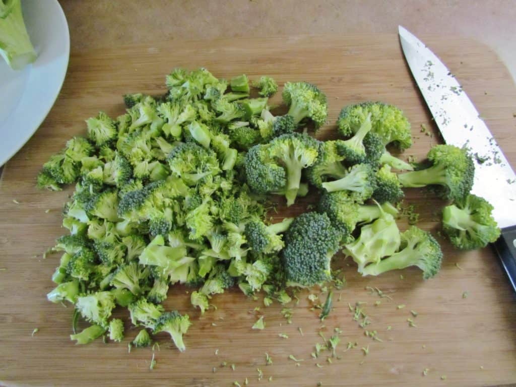 chopped broccoli florets on wooden cutting boards with chef's knife