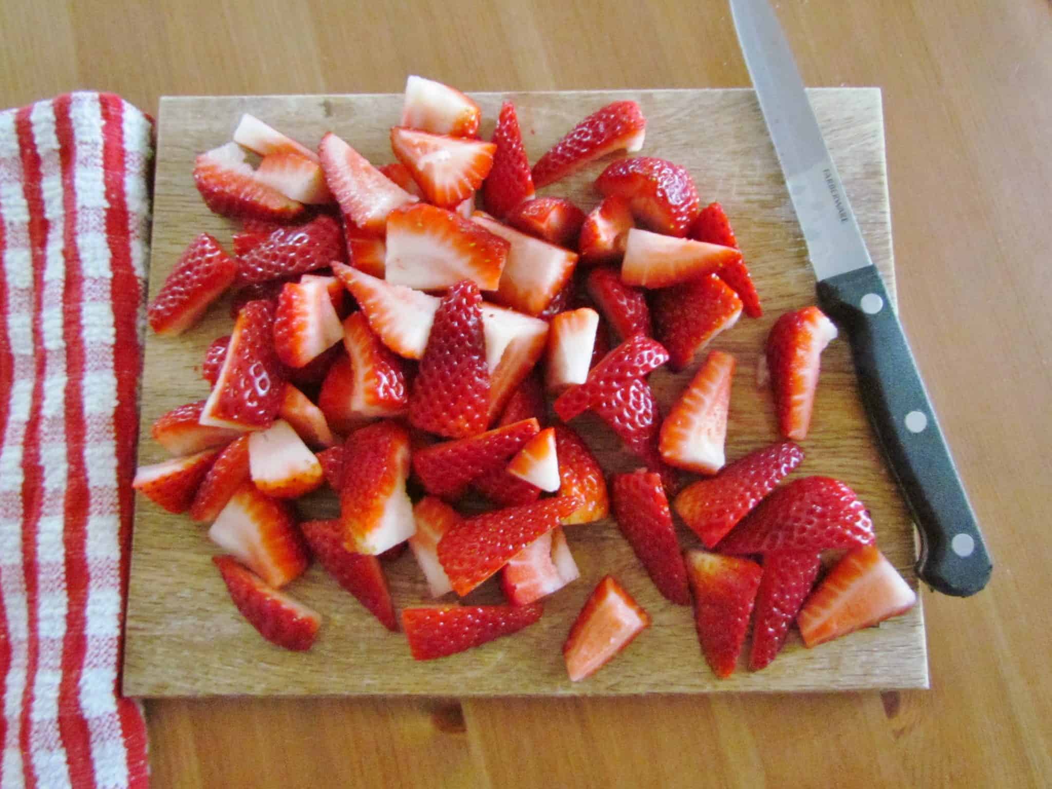sliced strawberries on a wooden cutting board.