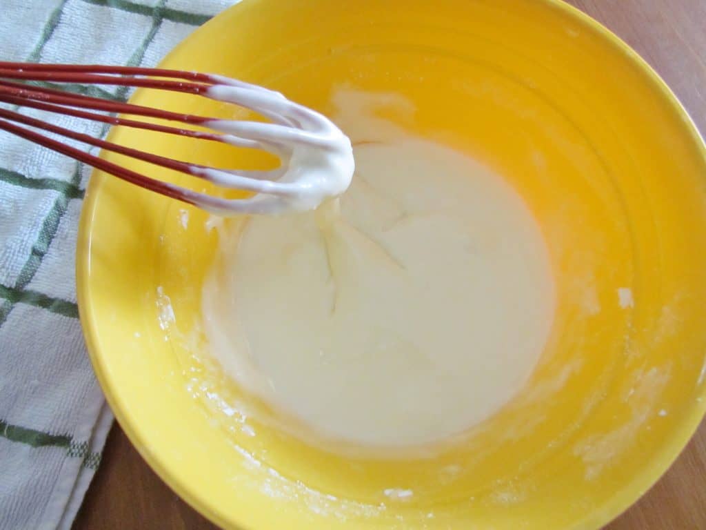 powdered sugar and milk whisked together in a small yellow mixing bowl.