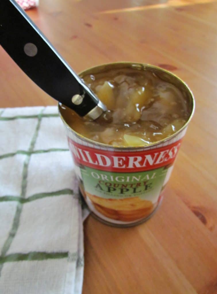 using a knife to slice apples in half inside a can of apple pie filling.