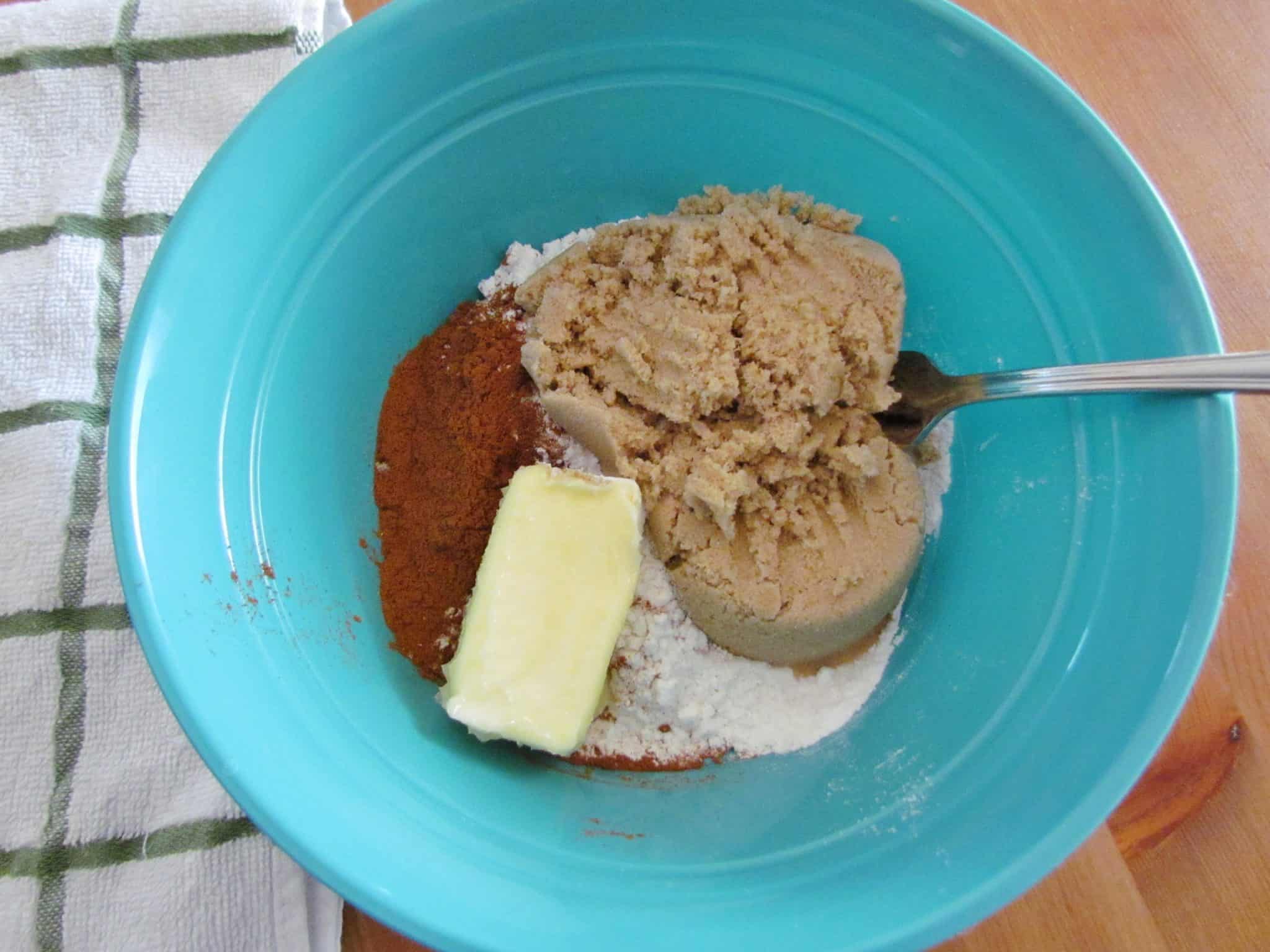 butter, brown sugar, flour and ground cinnamon in a blue mixing bowl with a fork.