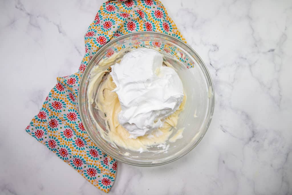 Cool Whip whipped topping added to cream cheese mixture in a clear bowl