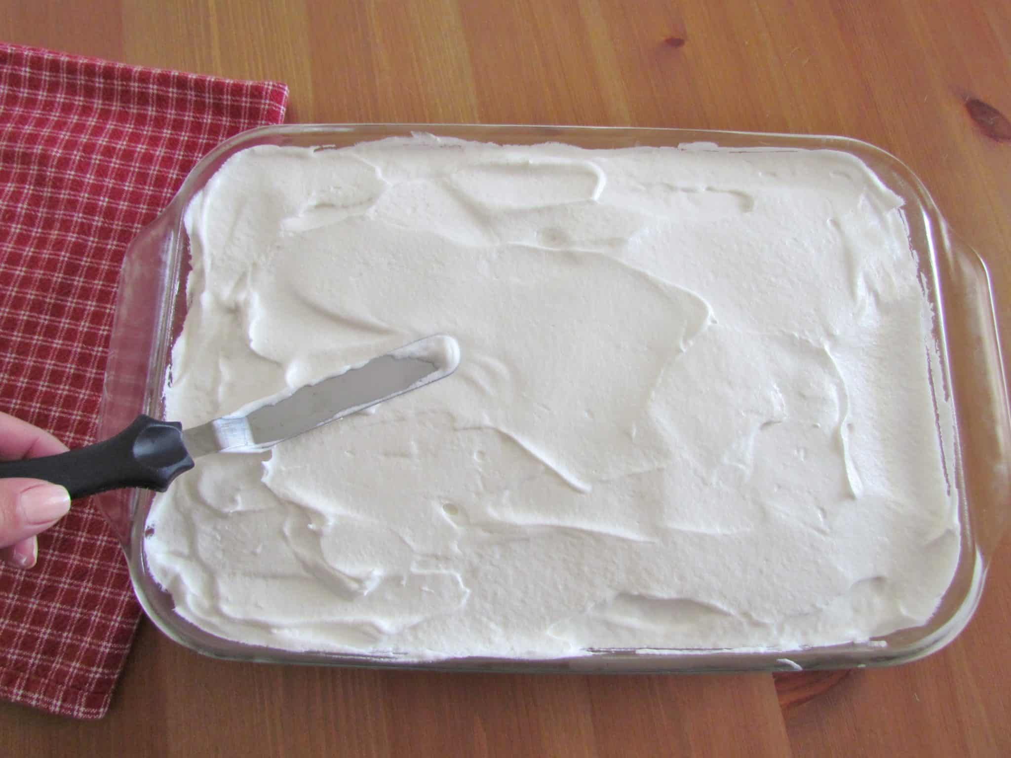 an offset spatula spreading Cool Whip on top of white cake