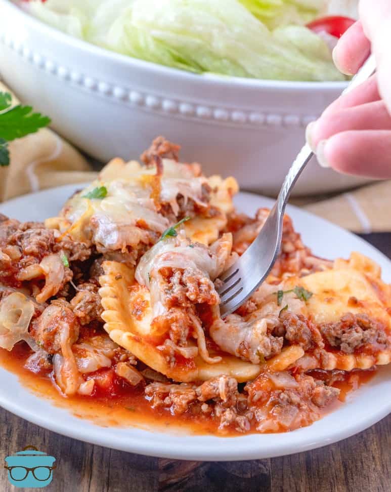 Baked Ravioli Casserole on a white plate, shown using a gork to pick up a ravioli from the plate