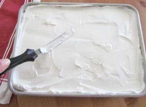 spreading whipped topping on top of cooled cake.