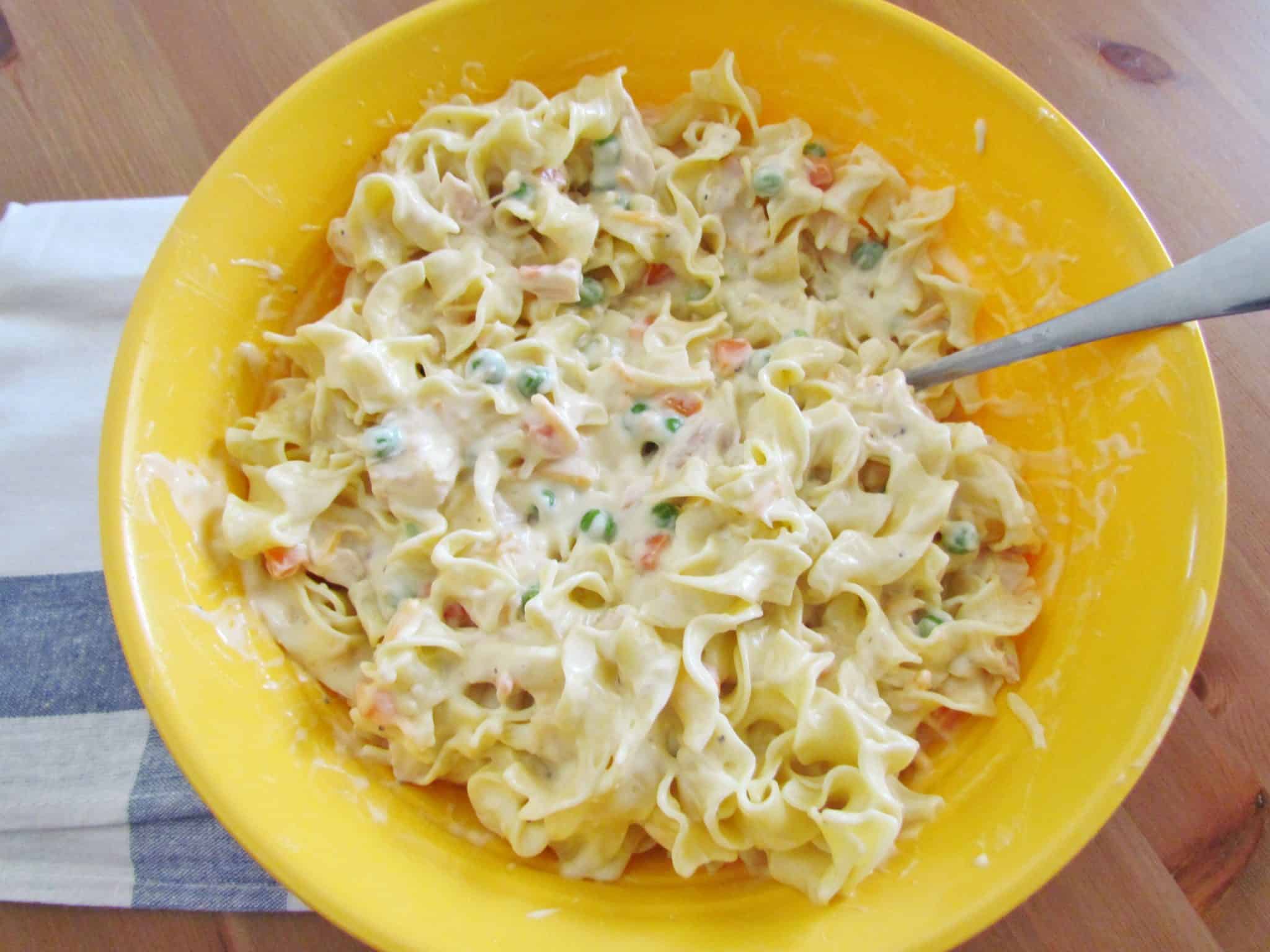 egg noodles stirred in with creamy filling mixture in a bowl.
