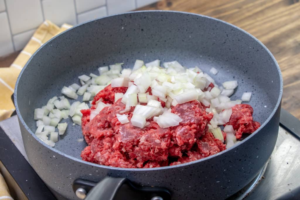 ground beef and diced onion in a large grey skillet