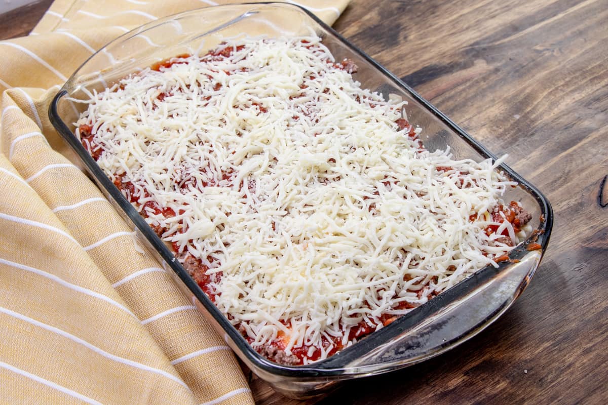 shredded cheese added on top of ravioli casserole layers in baking dish.