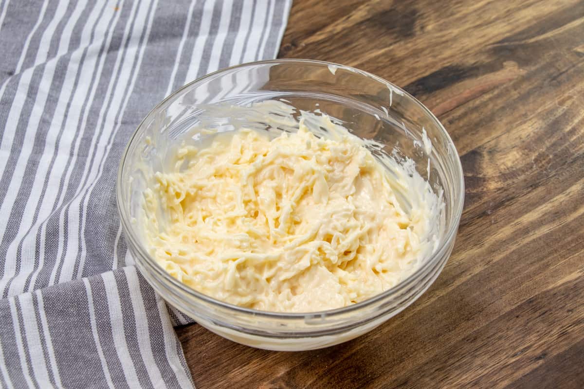 sliced cheese and mayonnaise mixed together in a glass bowl.
