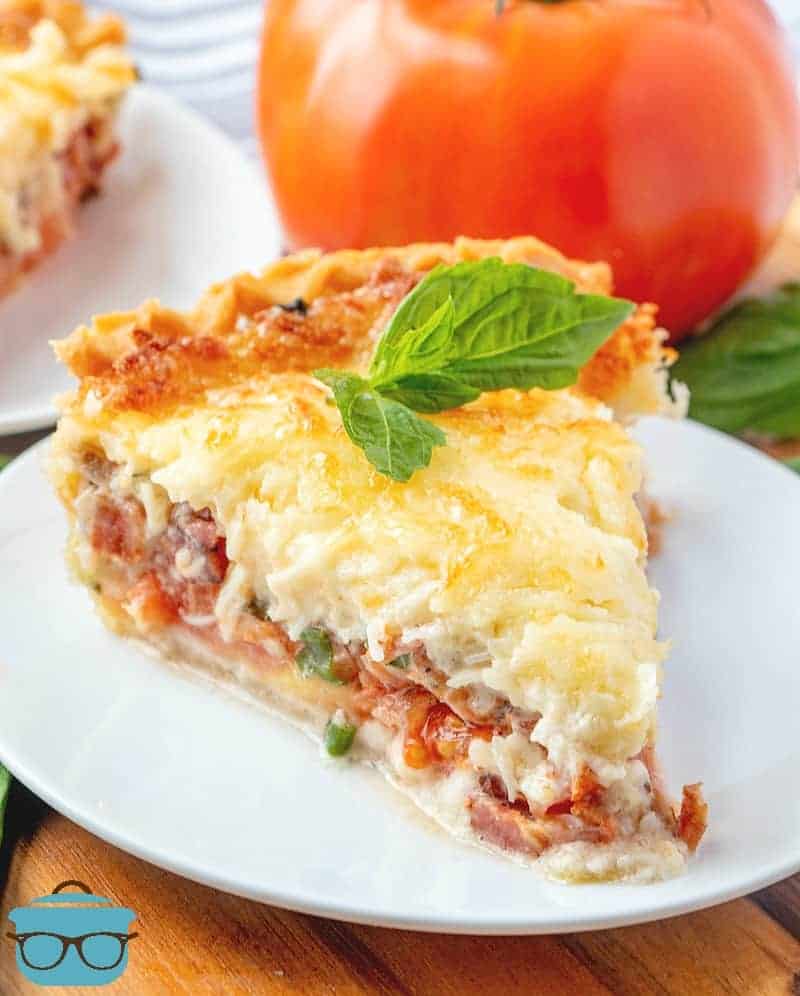 Tomato and Bacon Pie topped with melted mozzarella served on a white plate with a sprig of basil on top