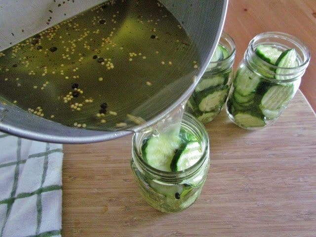 pickling brine poured over sliced cucumbers in mason jars