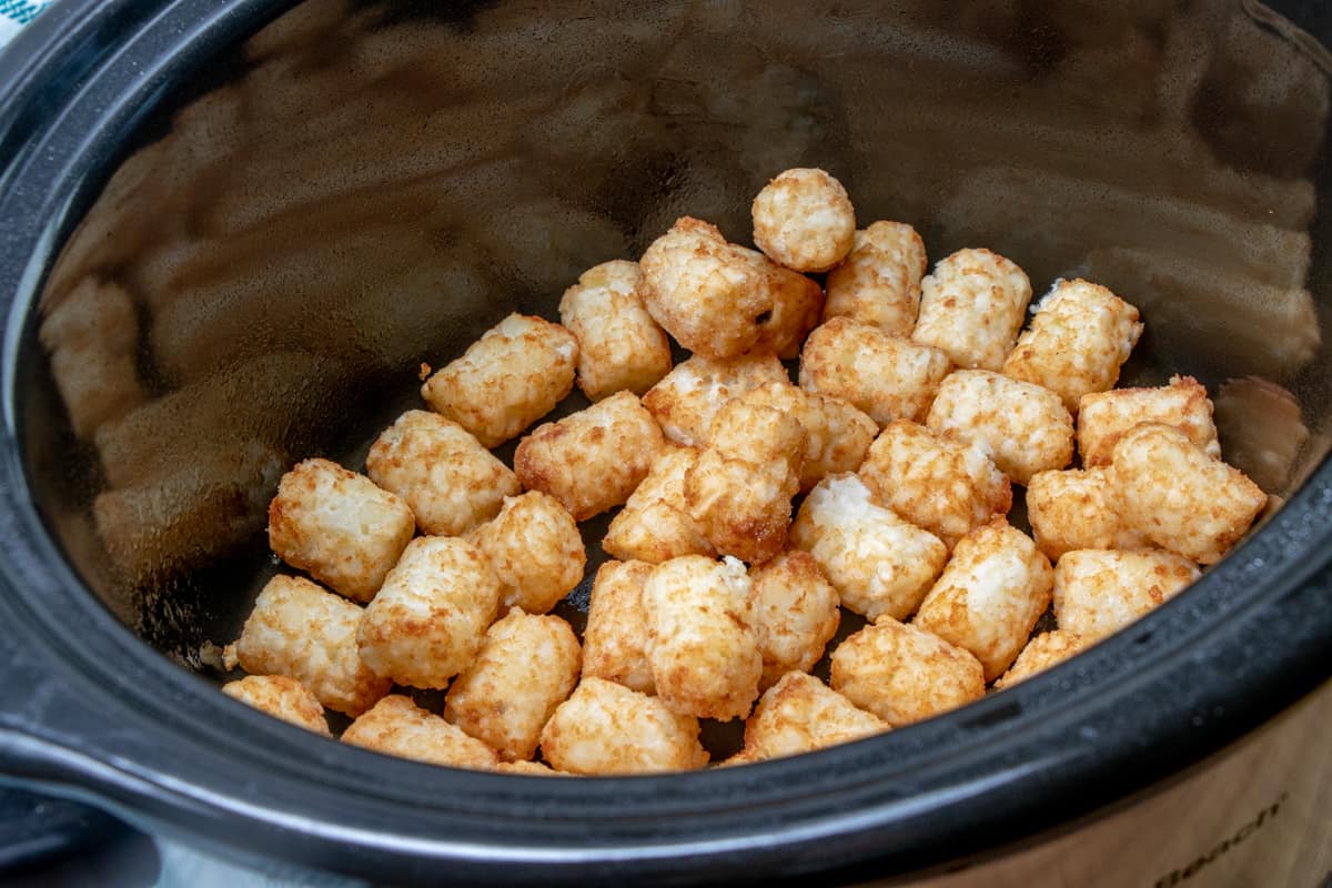 layering the bottom of a slow cooker with tater tots.