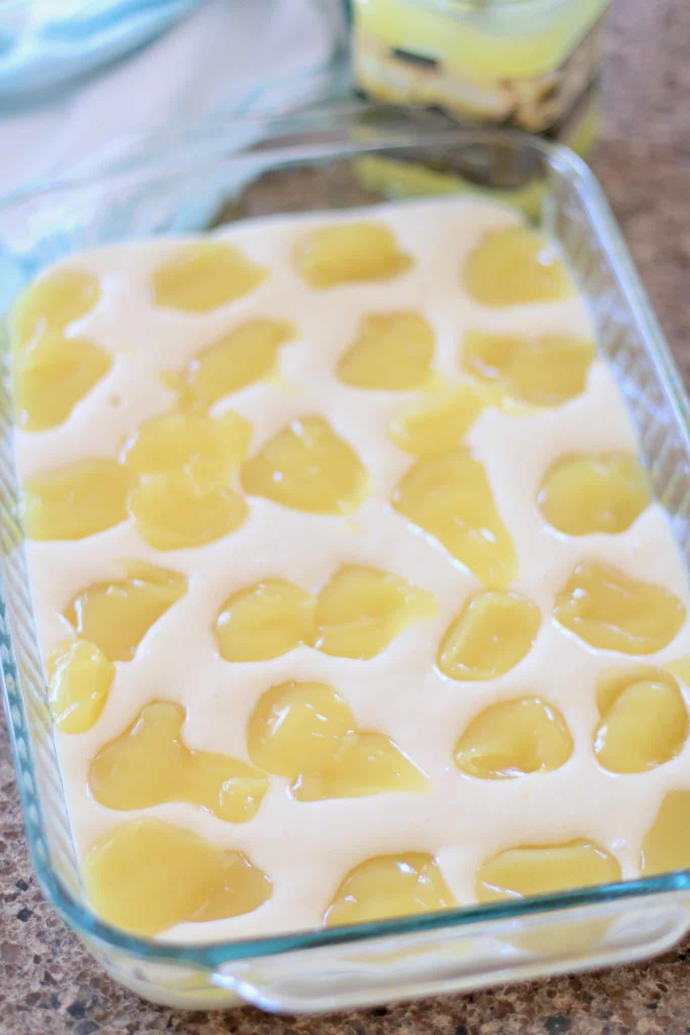 vanilla cake batter in a glass baking dish with pie filling dotted all over the cake batter.