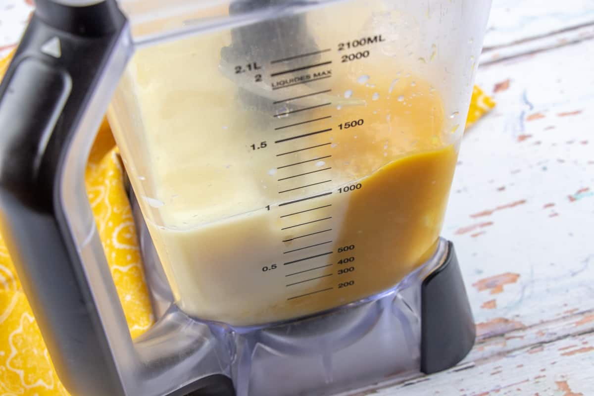 milk, orange juice concentrate, vanilla and sugar shown in the bottom of a blender.