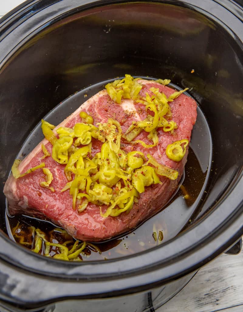 chuck roast, beef broth, Italian dressing seasoning and pepperoncini in an oval slow cooker