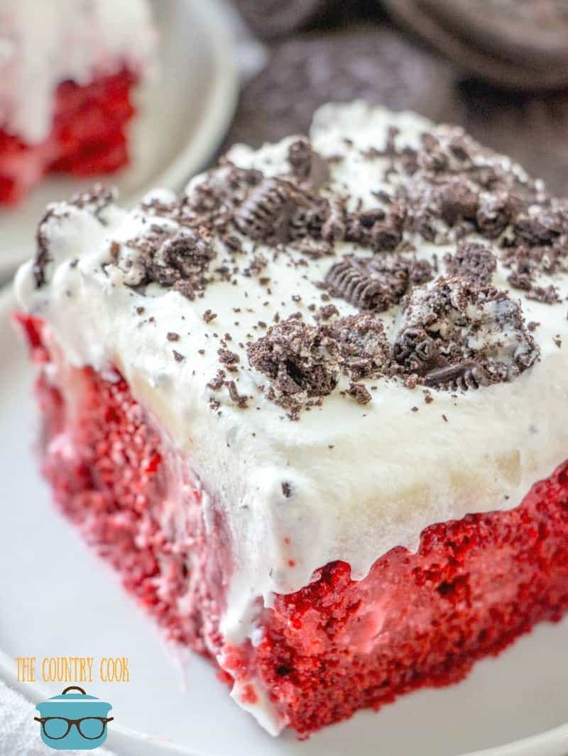 close up photo of a slice of red velvet poke cake topped with crushed Oreo cookies.