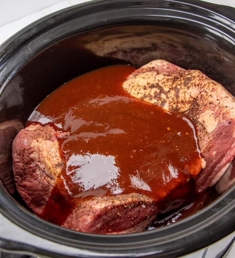 homemade barbecue sauce poured over seasoned beef brisket in a 6 quart oval slow cooker