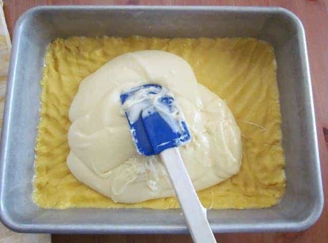 a spatula spreading cream cheese batter on top of cake mix in baking pan.