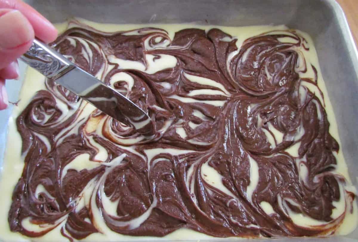 a knife swirling chocolate batter around into the cream cheese mixture. 