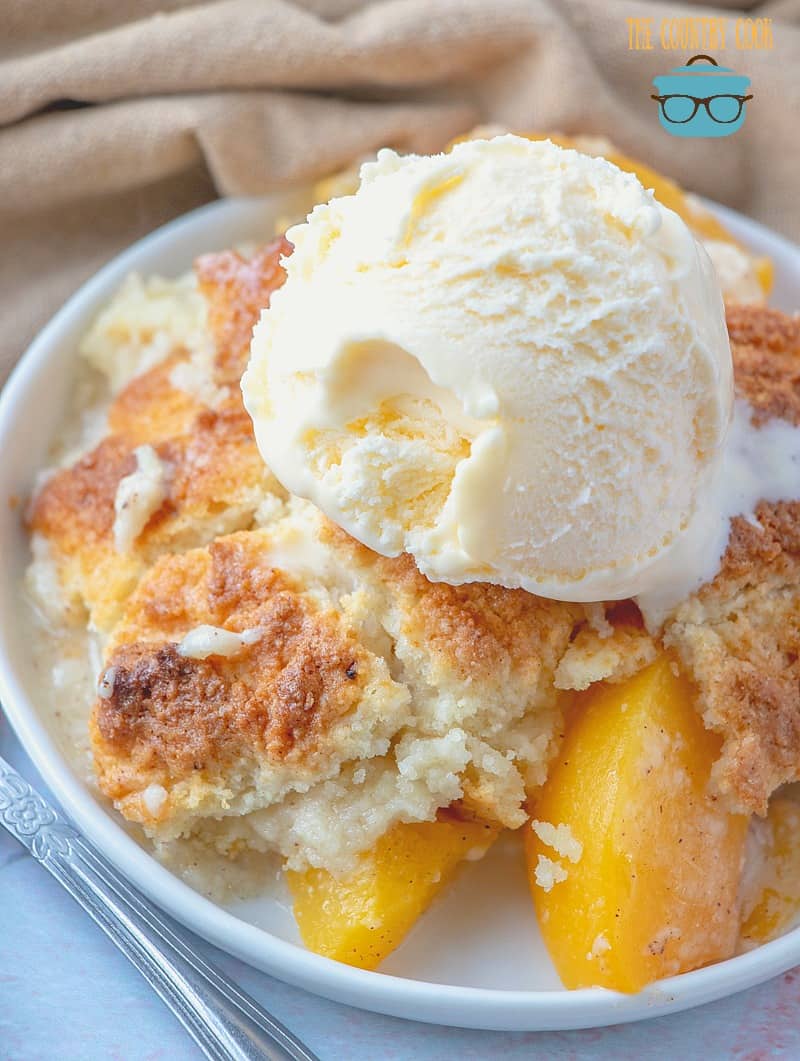 Photo of Country Peach Cobbler served in a shallow white bowl with a scoop vanilla ice cream on top - by The Country Cook