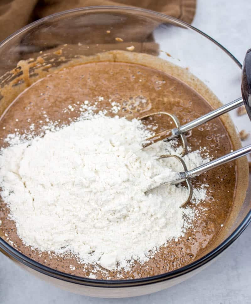 all purpose flour added to chocolate batter in a bowl.