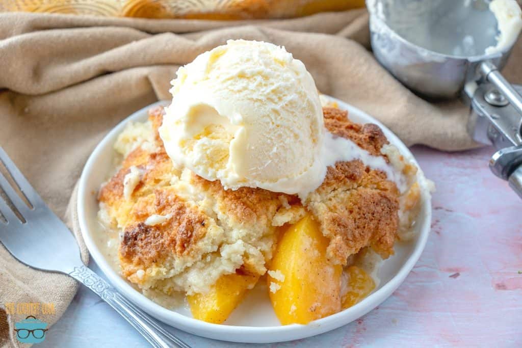 Easy Country Peach Cobbler topped with vanilla ice cream on a plate.