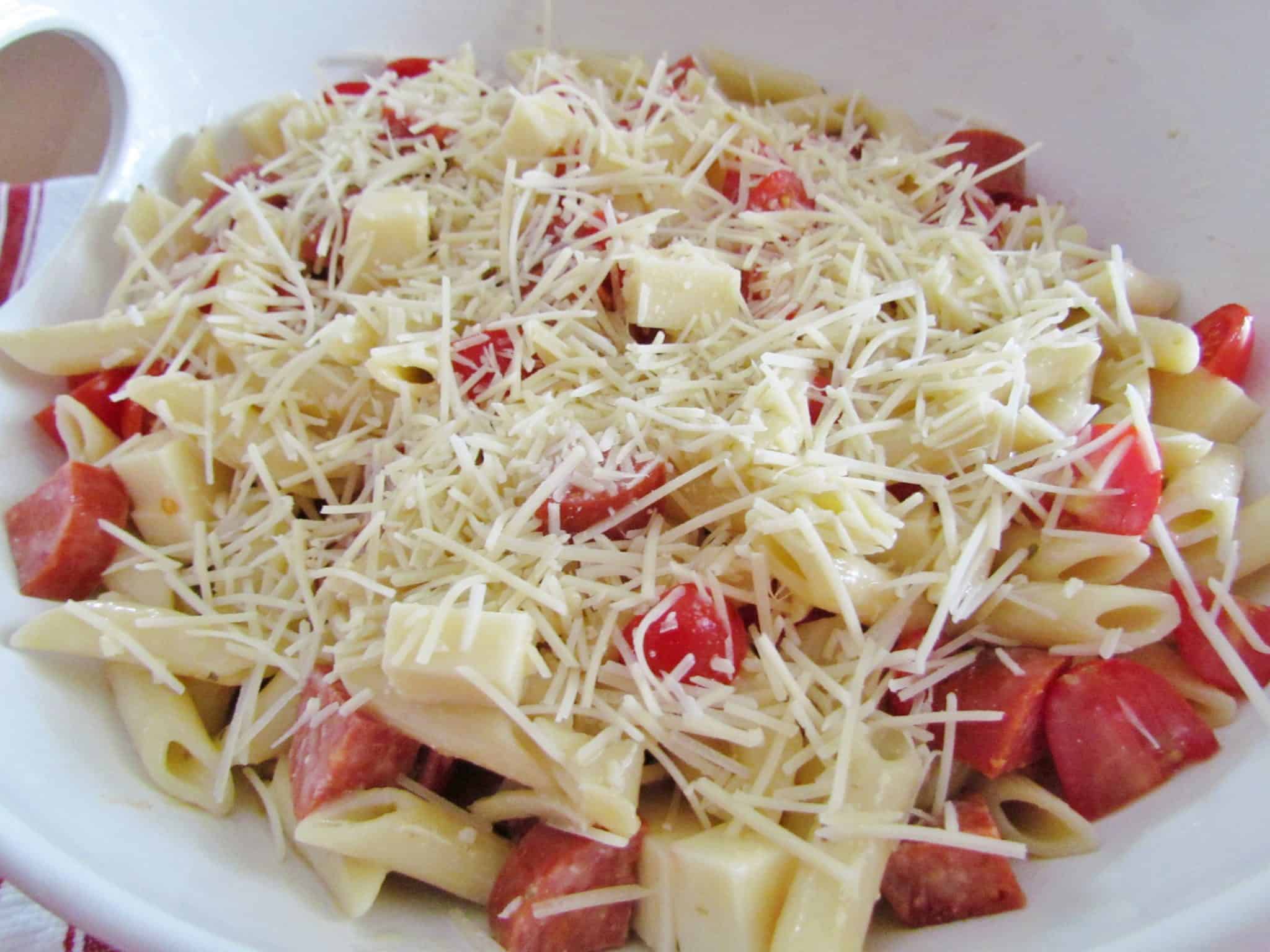 Parmesan cheese added to pepperoni pizza pasta salad in a white bowl.