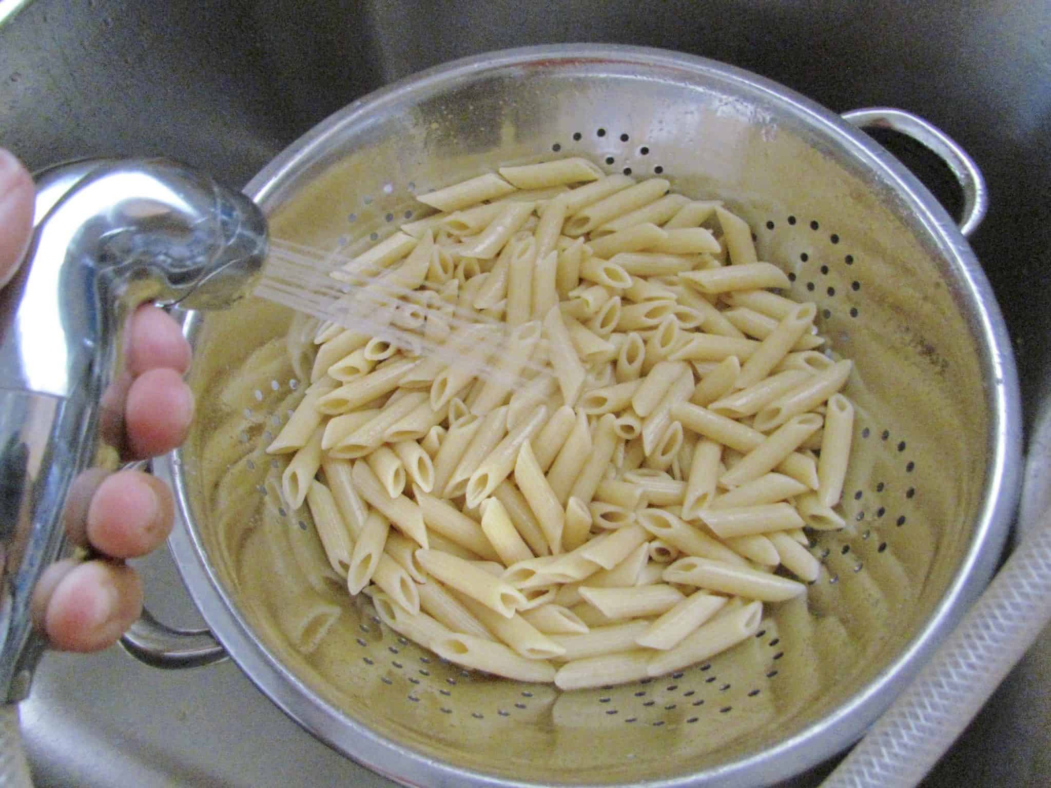 rinsing cooked penne pasta in a silver colander.