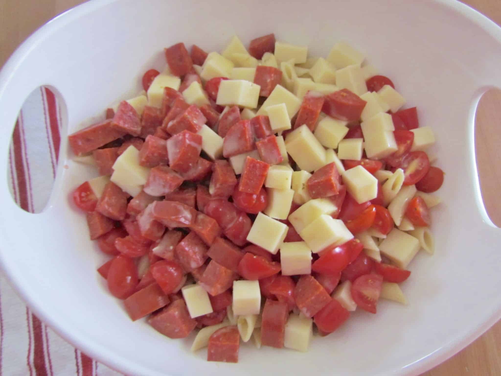cooled penne pasta, diced mozarella, sliced tomatoes and diced pepperoni in a large bowl.